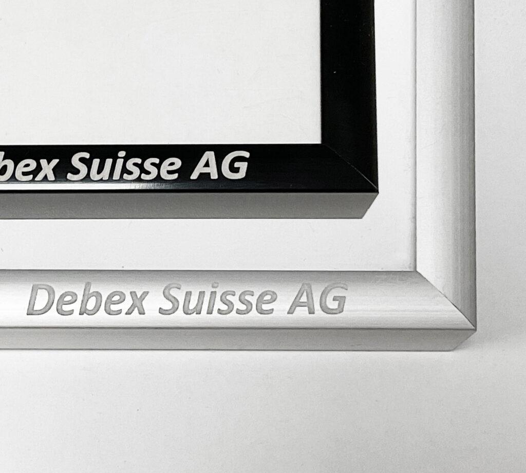 Close-up of laser engraving on a silver metal frame and custom printing on a black frame for Debex Suisse AG.
